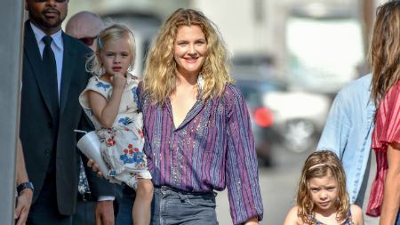 drew holding on baby on her arm and holding the others hand walking on the street 